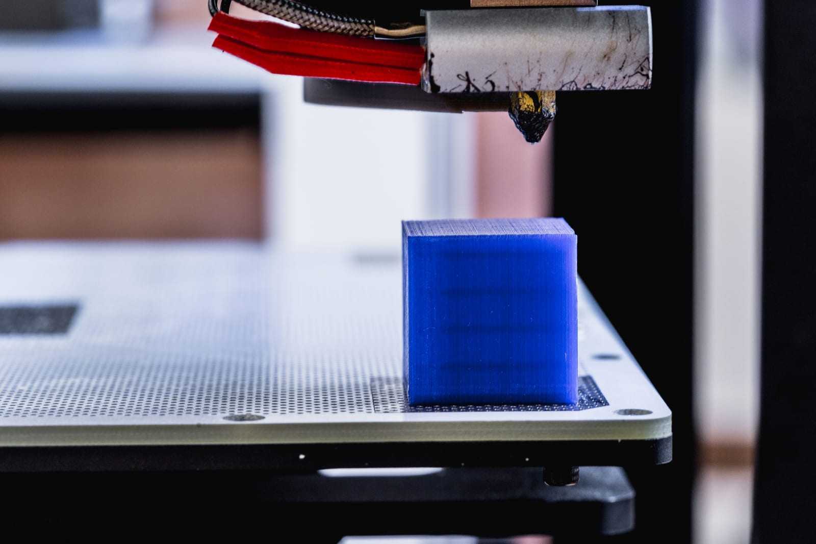 Bico de impressora 3D finalizando uma peça sobre a mesa perfurada